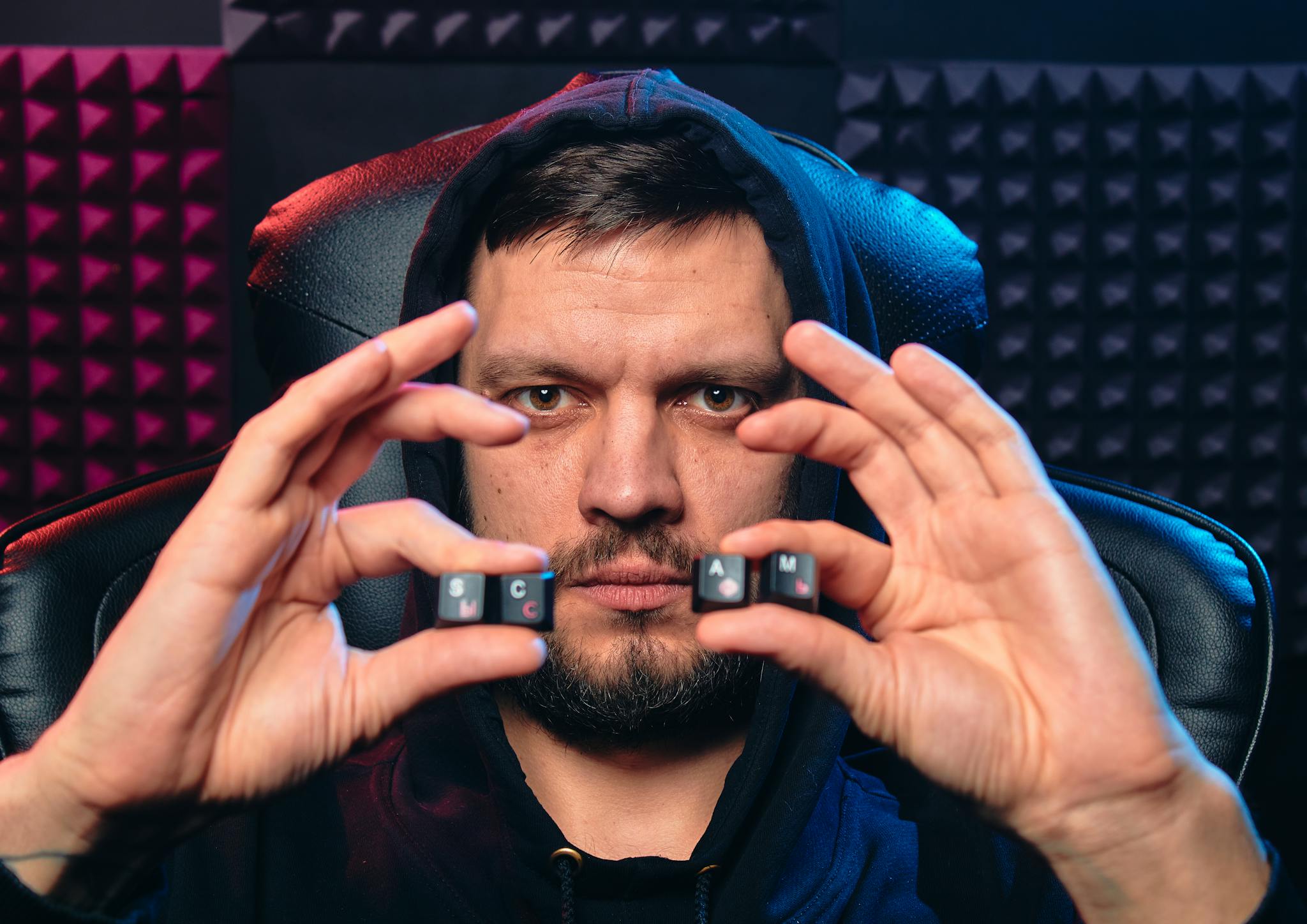 Man in hoodie holding alphabet keys spelling 'SCAM', symbolizing cybersecurity threat.